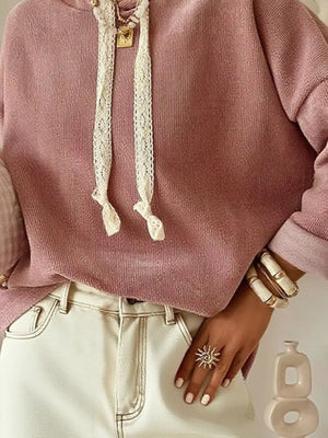 Woman wearing a pink knit sweater, cream jeans, chunky bracelets, sun ring, and necklace