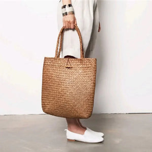 Woman holding woven straw tote bag, wearing light outfit and white shoes