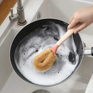 Handwashing a frying pan with a natural bristle dish brush in a sink with soapy water