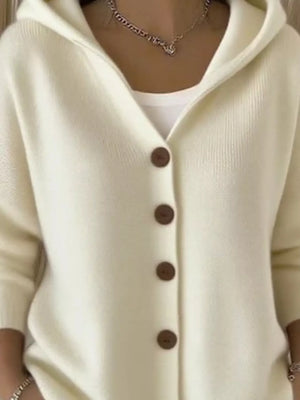 Woman wearing cream knit hooded cardigan with brown buttons, layered over white top
