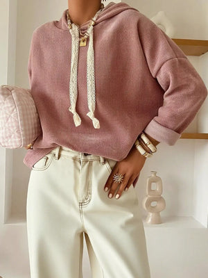 Woman wearing a pink hoodie with lace drawstrings, cream high-waist pants, and gold jewelry.