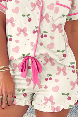 Woman wearing white pajama set with pink bows, hearts, cherries, and pink trim details.