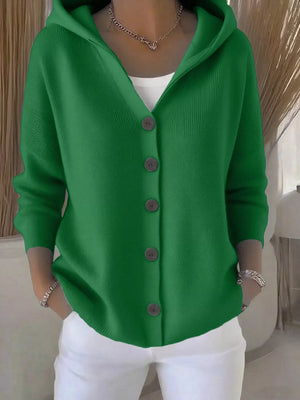 Woman wearing a green button-up hooded cardigan with white pants and a necklace