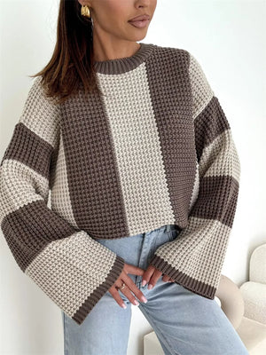 Woman wearing a chunky knit brown and beige striped sweater with wide sleeves and light jeans