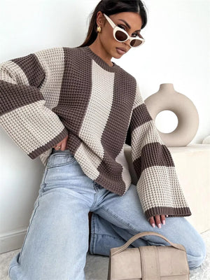 Woman wearing oversized striped knit sweater, light wash jeans, sunglasses, and holding beige handbag