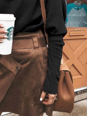 Woman wearing black ribbed sweater, brown suede skirt, tan leather handbag, holding coffee cup