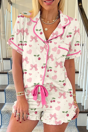 Woman wearing short-sleeve pajama set with pink bows, hearts, and cherry print details