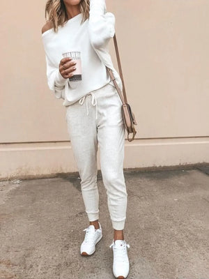 Woman in casual off-shoulder white sweater, joggers, sneakers, holding coffee