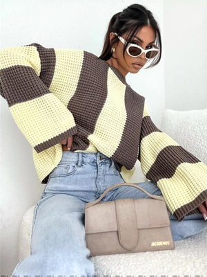 Woman in oversized striped sweater, light blue jeans, sunglasses, with taupe Jacquemus handbag