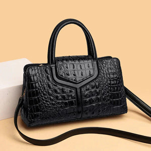 Black crocodile pattern leather handbag with top handle and shoulder strap on beige background