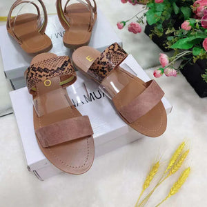 Women's open-toe flat sandals with suede and snakeskin patterned straps on display boxes