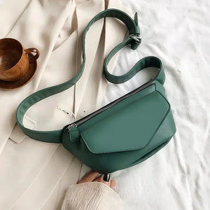 Sage green crossbody bag with zipper on neutral fabric, wooden cup beside it