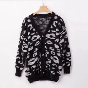 Black fuzzy cardigan with white animal print pattern and button front, hanging on hanger