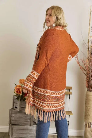 Woman modeling orange knit cardigan with fringe hem and patterned trim, casual home setting