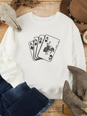 White sweatshirt with playing cards graphic, paired with blue jeans and suede boots