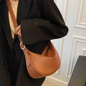 Woman in black blazer carrying a brown leather crescent shoulder bag