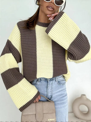 Woman in oversized yellow and brown striped knit sweater with blue jeans and beige handbag