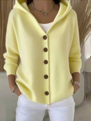 Woman wearing a pastel yellow hooded cardigan with brown buttons and white pants