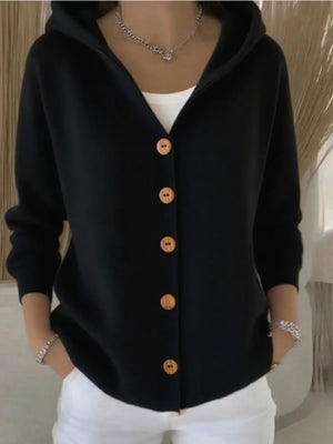 Woman wearing a black hooded cardigan with brown buttons and white pants, casual style