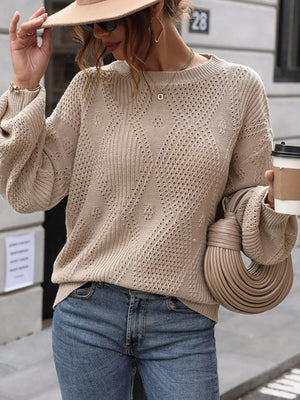 Woman in beige knit sweater, blue jeans, holding coffee and taupe handbag on city street