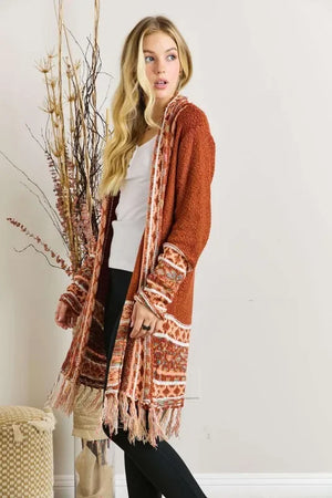 Woman wearing a rust-colored knit cardigan with fringe and patterned sleeves, casual outfit.