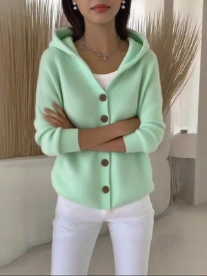 Woman wearing a light green hooded cardigan with buttons and white pants indoors