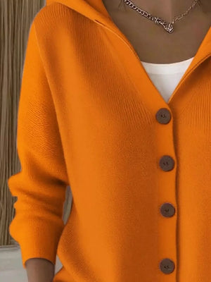 Woman wearing orange button-up knit cardigan with white top and chain necklace