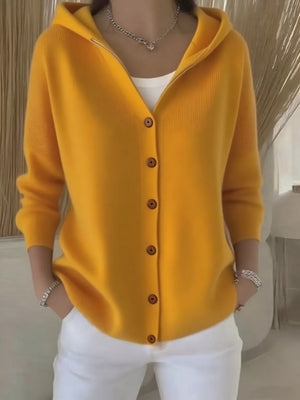 Woman wearing yellow button-up hooded cardigan with white pants and silver jewelry