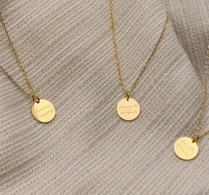 Gold engraved pendant necklaces with inspirational words displayed on beige fabric