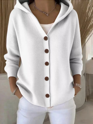 Woman wearing a white knit button-up hoodie cardigan with brown buttons and white pants