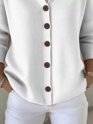 Woman wearing a white knit cardigan with brown buttons and white pants, casual fashion style