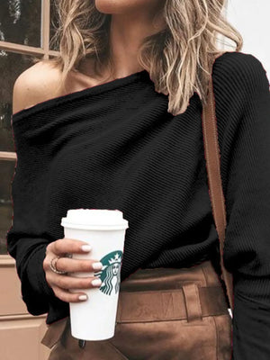 Woman in a black off-shoulder ribbed sweater with tan pants, holding a coffee cup