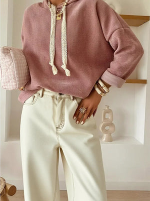 Woman wearing mauve hoodie and cream wide-leg pants with layered necklaces and gold bracelets