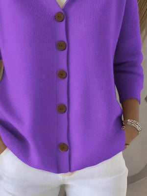 Woman wearing a purple button-up cardigan with white pants and layered bracelets