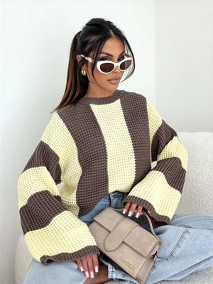 Woman wearing oversized brown and yellow striped knit sweater, light jeans, white sunglasses, and holding a beige Jacquemus handbag.