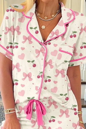 Woman wearing short-sleeve pajamas with pink bows, hearts, and cherry print, pink trim
