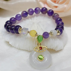 Purple beaded bracelet with multicolor gemstone charm and gold accents on white fabric.