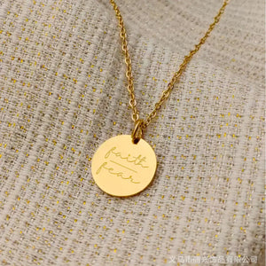 Gold round pendant necklace engraved with 'faith over fear' on textured fabric background