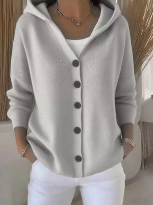 Woman wearing a light grey buttoned hooded cardigan over a white top and white pants