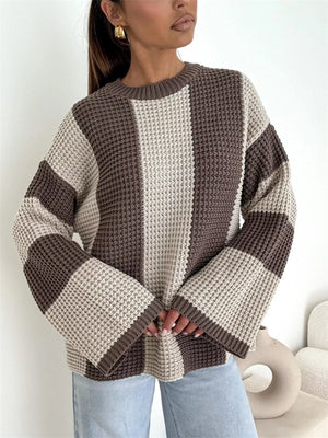 Woman wearing a beige and brown colorblock knit sweater with wide sleeves and light blue jeans