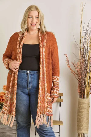 Smiling woman wearing a rust orange knit cardigan with fringe, black top, and blue jeans