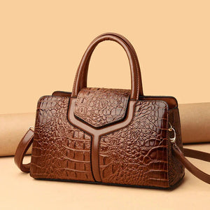 Brown crocodile-embossed leather handbag with top handles and shoulder strap on beige background.