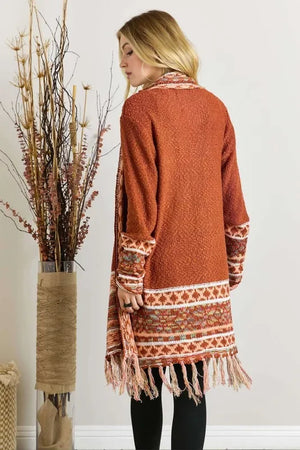 Woman wearing a rust orange knit cardigan with fringe and Nordic-inspired patterns