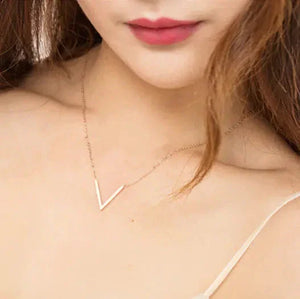 Minimalist gold V-shaped pendant necklace on woman with pink lips and light dress