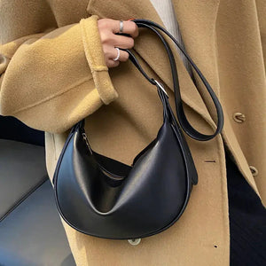 Woman wearing camel coat holding a black crescent shoulder bag with zipper