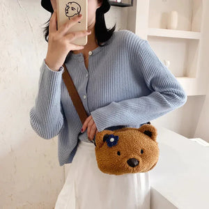 Woman wearing light blue ribbed sweater, white skirt, and brown bear-shaped crossbody bag.