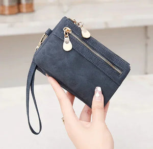 Woman holding a dark blue suede wristlet wallet with gold zippers and keychain detail