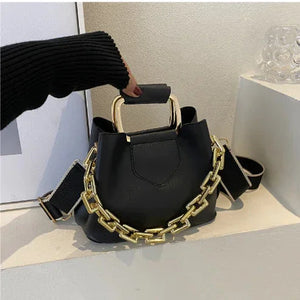 Black handbag with chunky gold chain, top handle, and wide shoulder strap on display