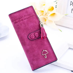 Purple suede wallet with umbrella charm, tassel, and button closure on white background