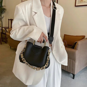 Woman in white blazer holding black handbag with gold chain strap in modern living room